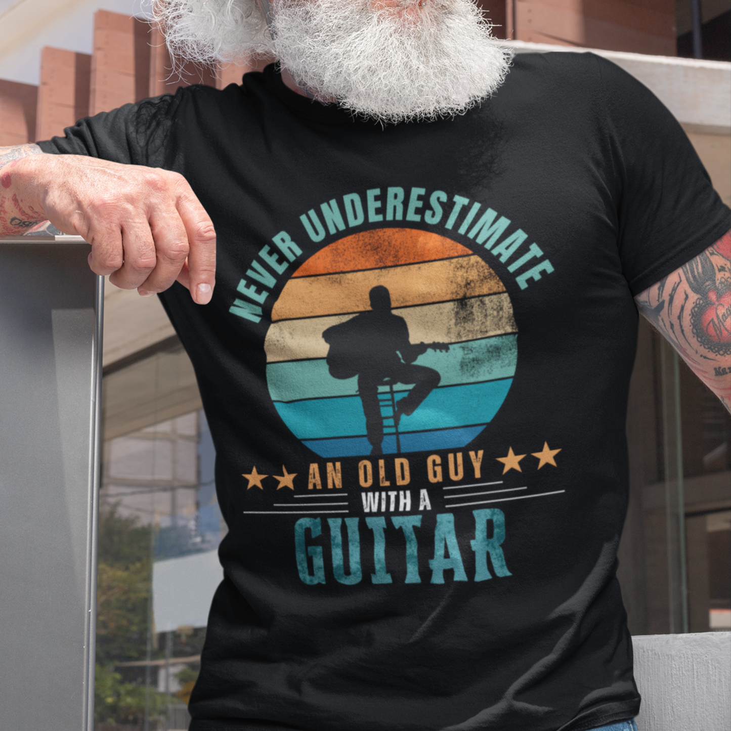Black tee featuring silhouette of a guy on a stool playing a guitar against a distressed striped sunset