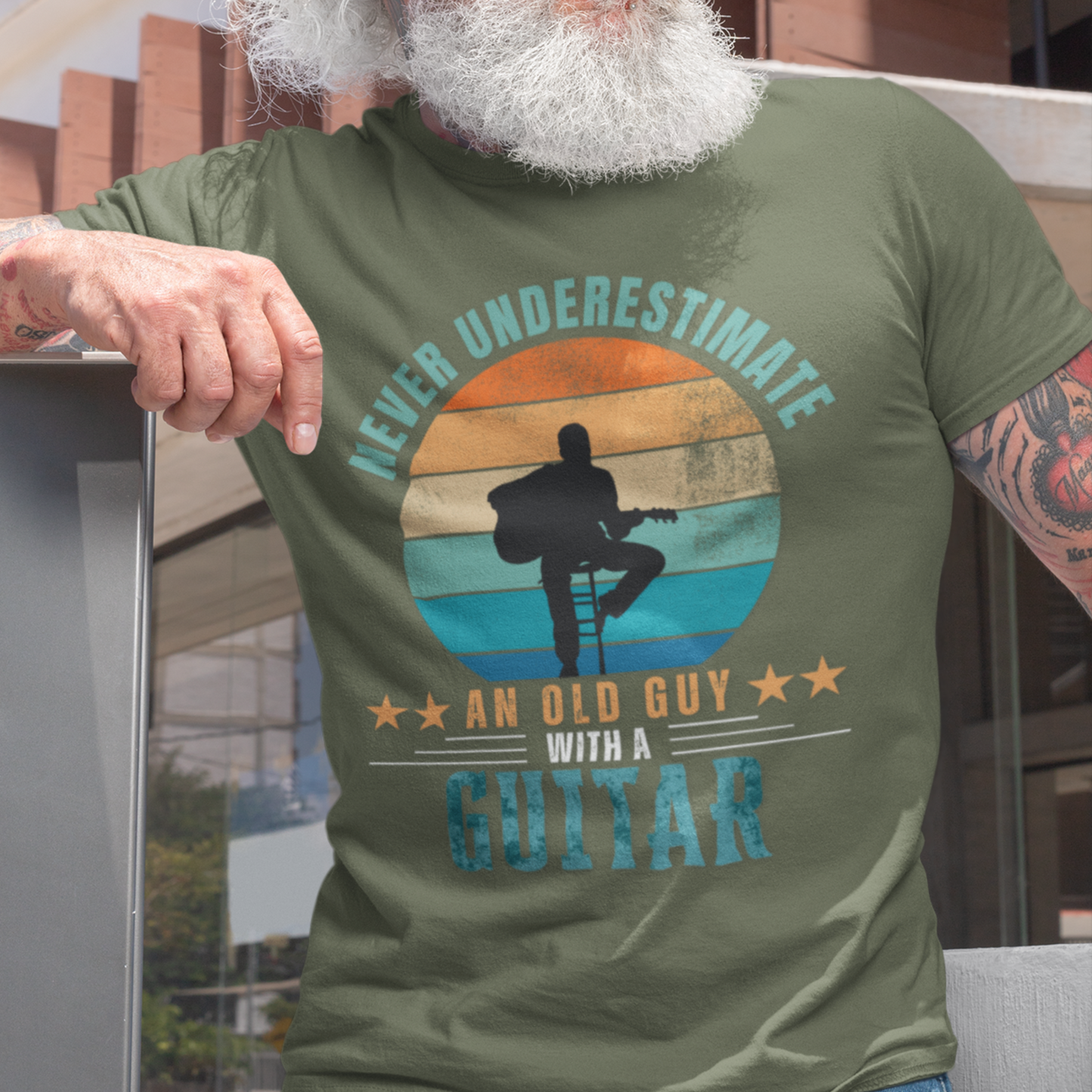 Military green tee featuring silhouette of a guy on a stool playing a guitar against a distressed striped sunset