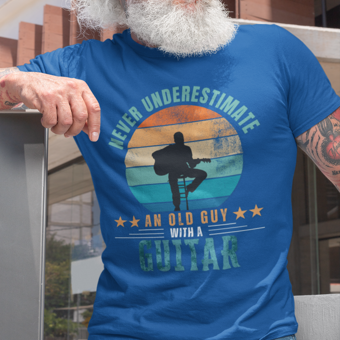 Royal blue tee featuring silhouette of a guy on a stool playing a guitar against a distressed striped sunset