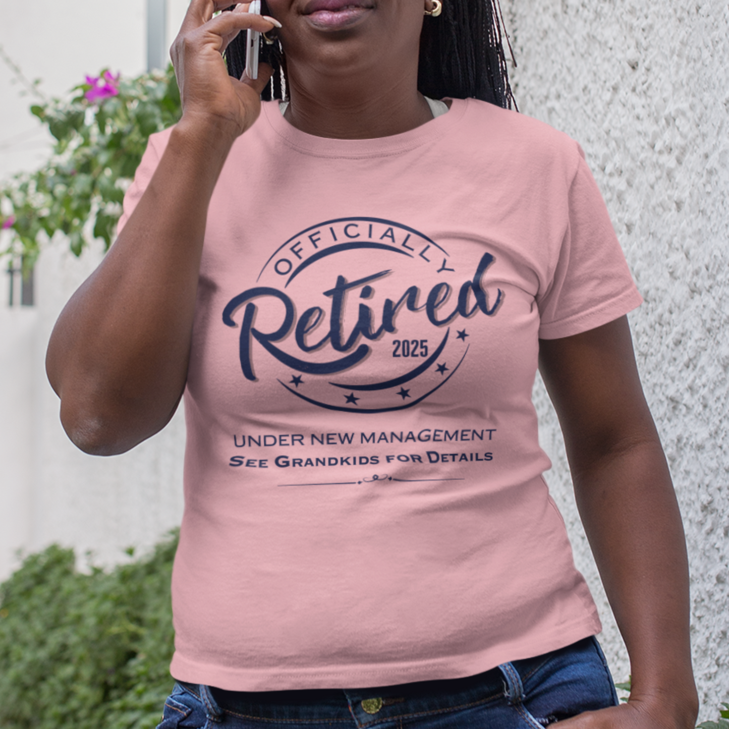 Light pink tee featuring a replica of an official stamp embossing that reads "Officially Retired 2025 See Grandkids" on a woman.