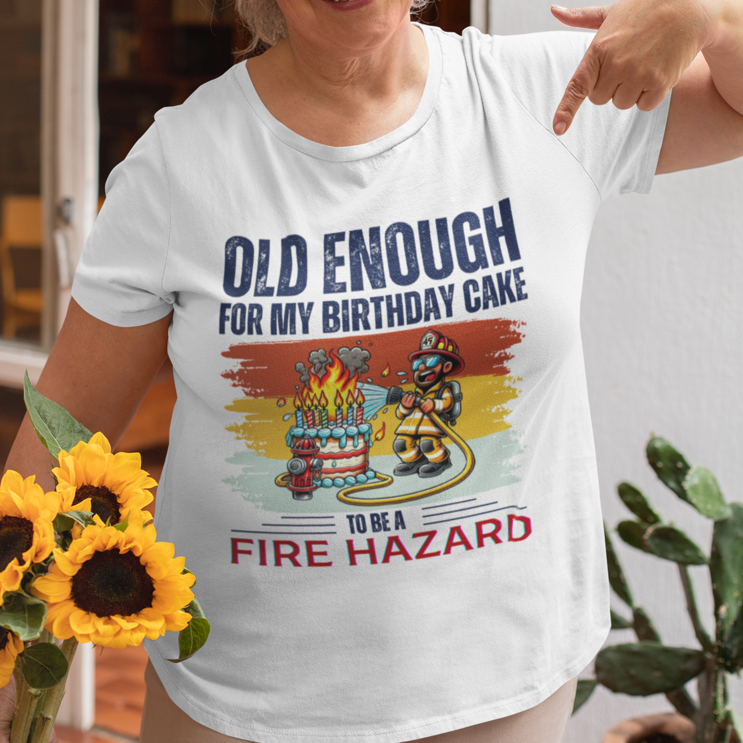 White tee featuring a cartoon fireman putting out the flames from the candles on a birthday cake.