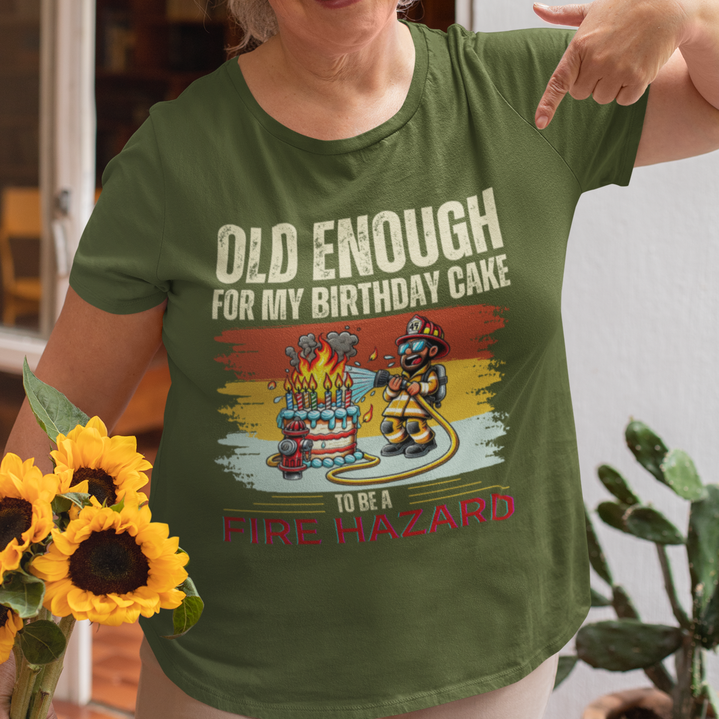 Military green tee featuring a cartoon fireman putting out the flames from the candles on a birthday cake.