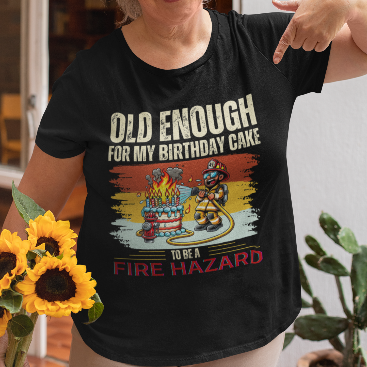 Black tee featuring a cartoon fireman putting out the flames from the candles on a birthday cake.