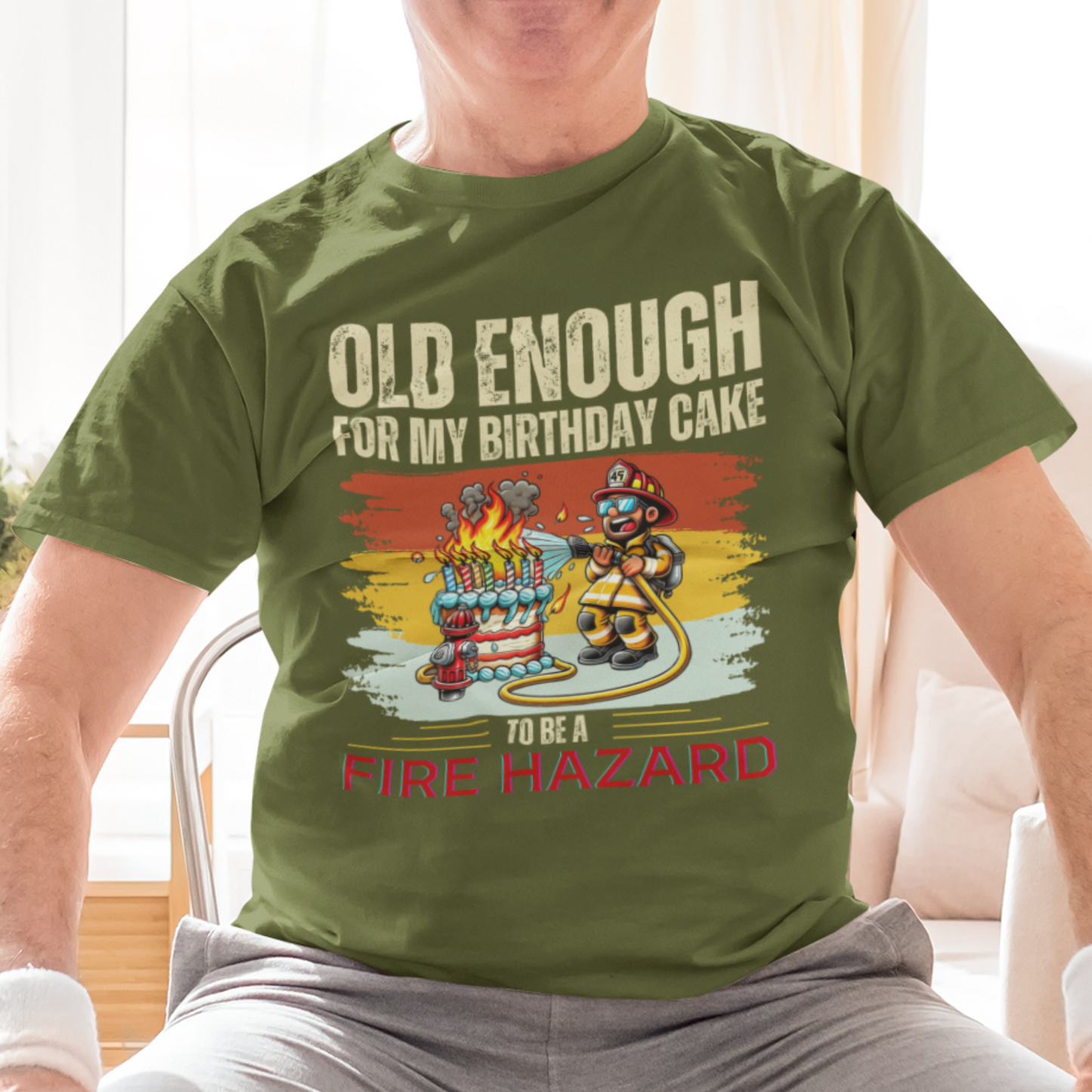 Military green tee featuring a cartoon fireman putting out the flames from the candles on a birthday cake.