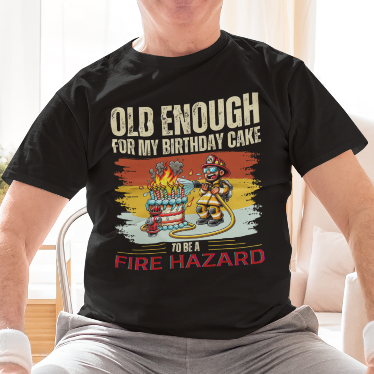 Black tee featuring a cartoon fireman putting out the flames from the candles on a birthday cake.