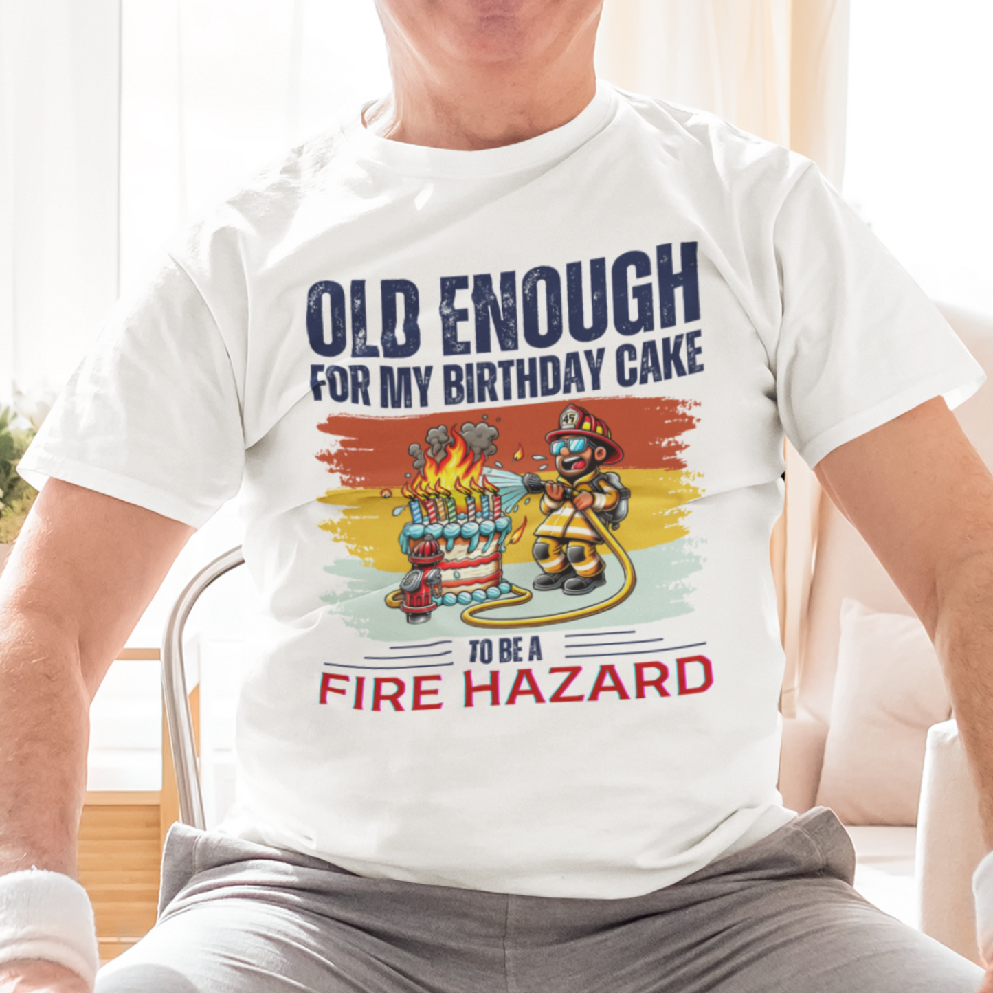 White tee featuring a cartoon fireman putting out the flames from the candles on a birthday cake.