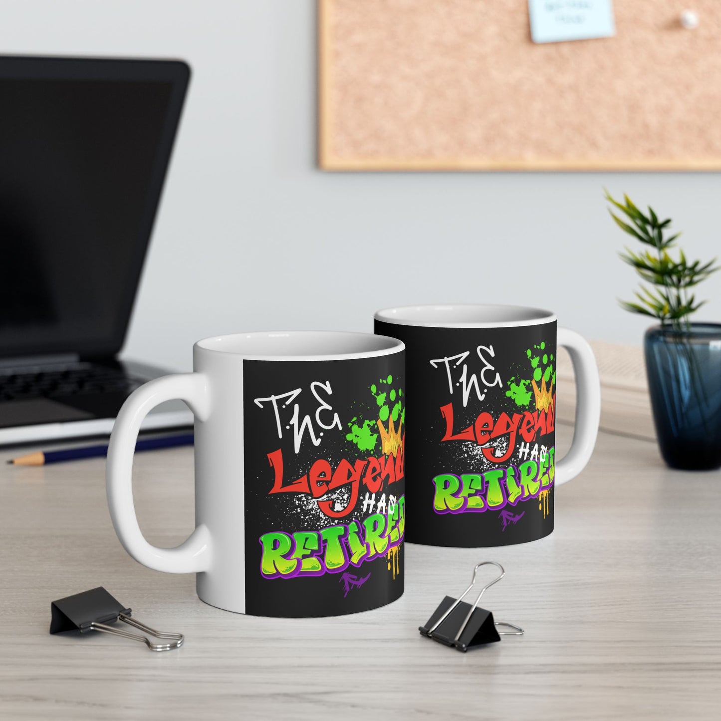 Two mugs with colorful text design on a desk with office items.