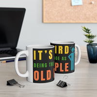 Two mugs with humorous text design on a desk with office supplies and a plant.