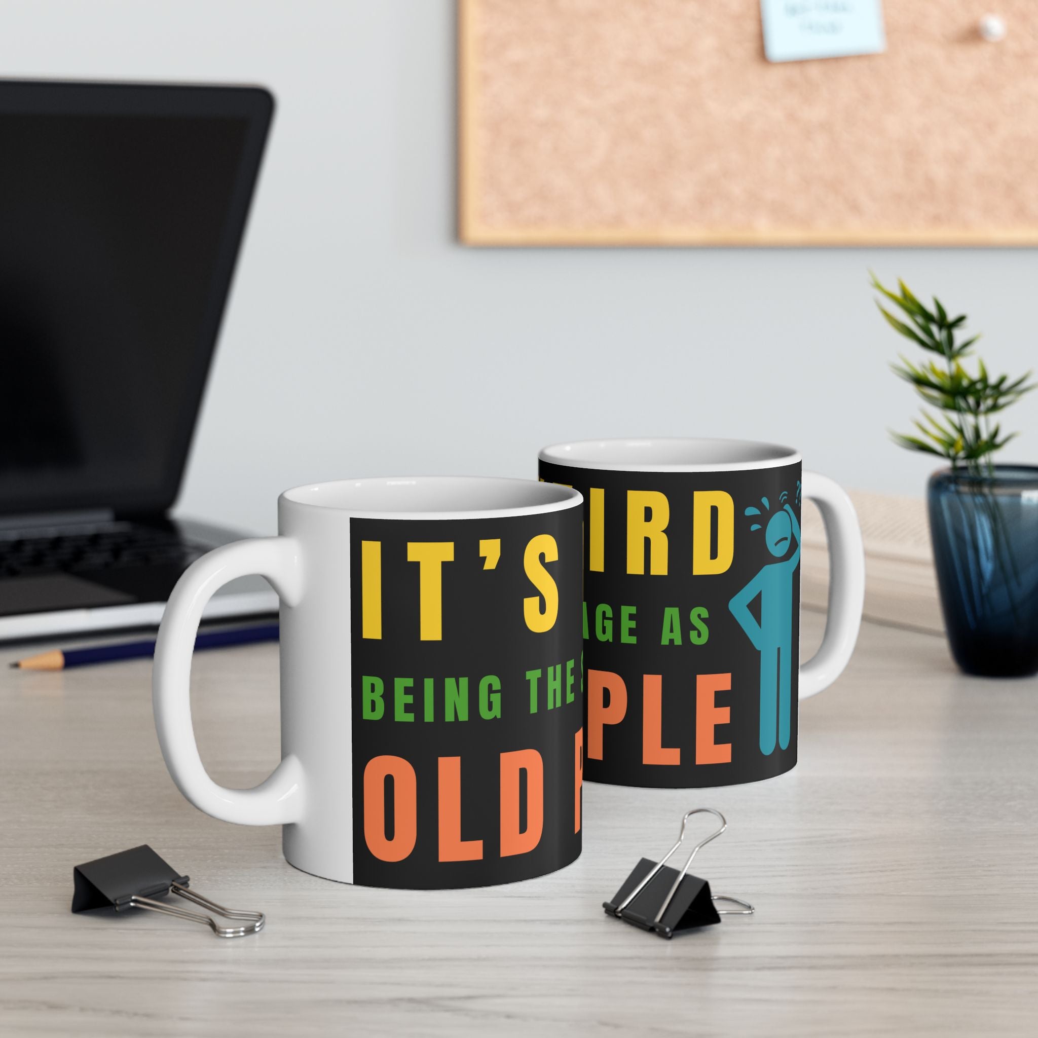 Two mugs with humorous text design on a desk with office supplies and a plant.