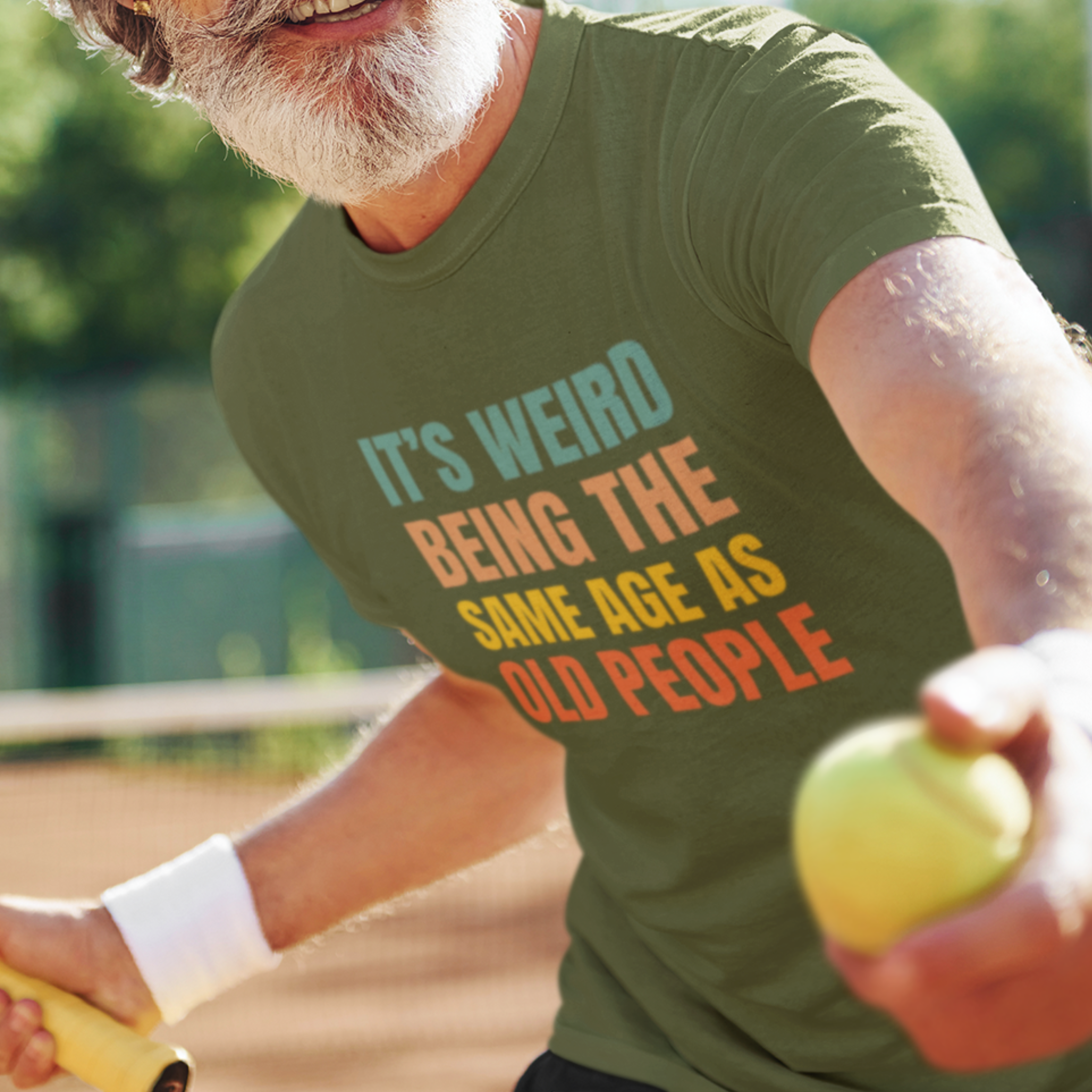 Military green tee featuring bold, rainbow-colored lettering reads It’s Weird Being the Same Age as Old People 