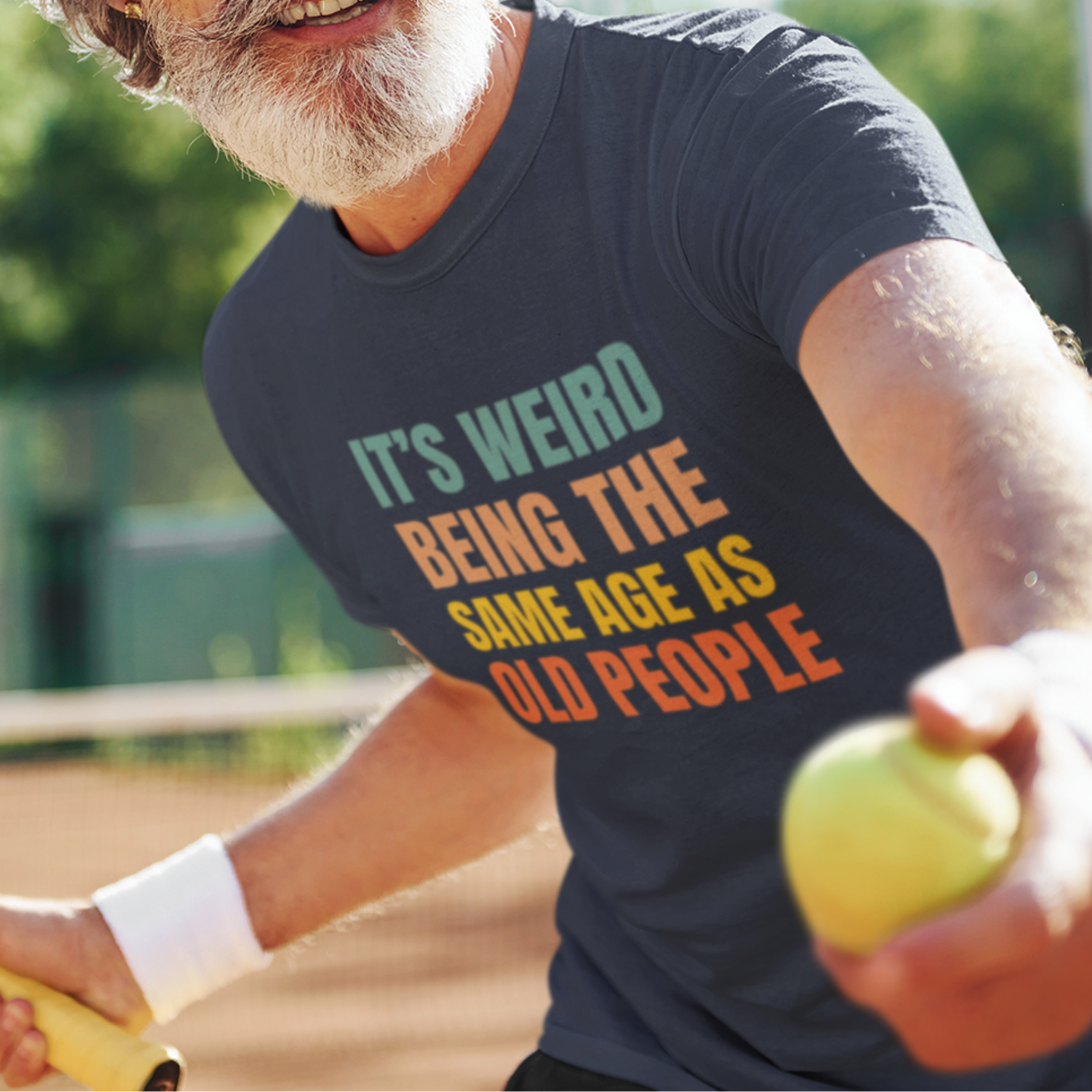 Navy blue tee featuring bold, rainbow-colored lettering reads It’s Weird Being the Same Age as Old People 