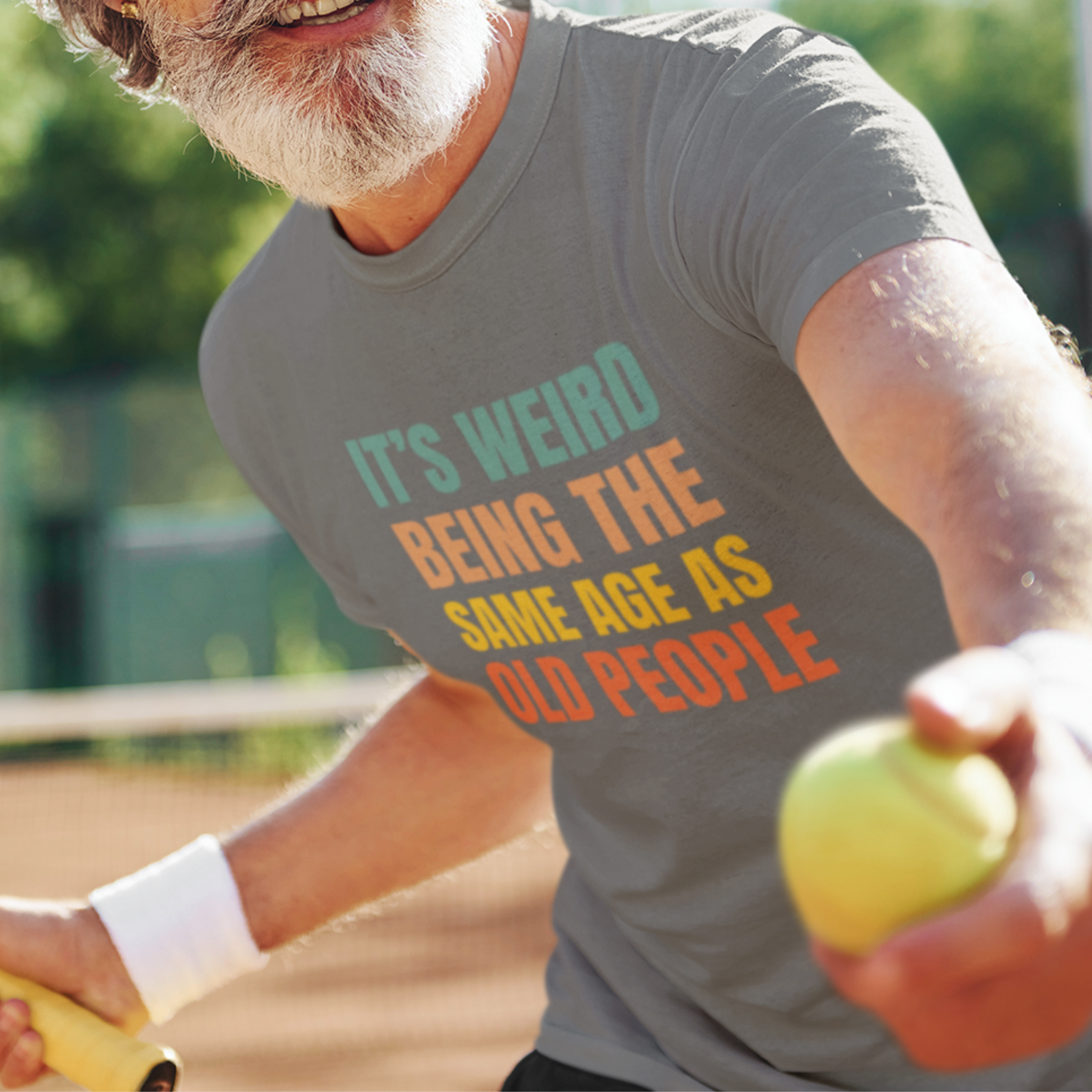 Gray tee featuring bold, rainbow-colored lettering reads It’s Weird Being the Same Age as Old People 