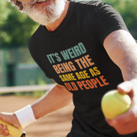 Black tee featuring bold, rainbow-colored lettering reads It’s Weird Being the Same Age as Old People 