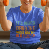 Royal blue tee featuring bold, rainbow-colored lettering reads It’s Weird Being the Same Age as Old People 