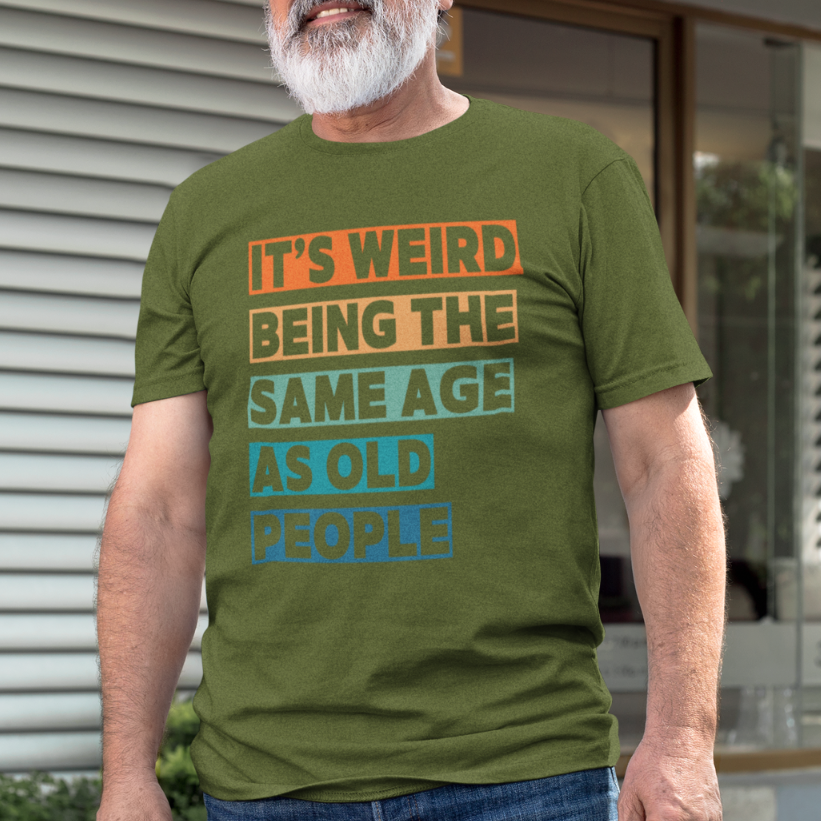 Military green tee featuring bold, multi-color block lettering reads It’s Weird Being the Same Age as Old People 