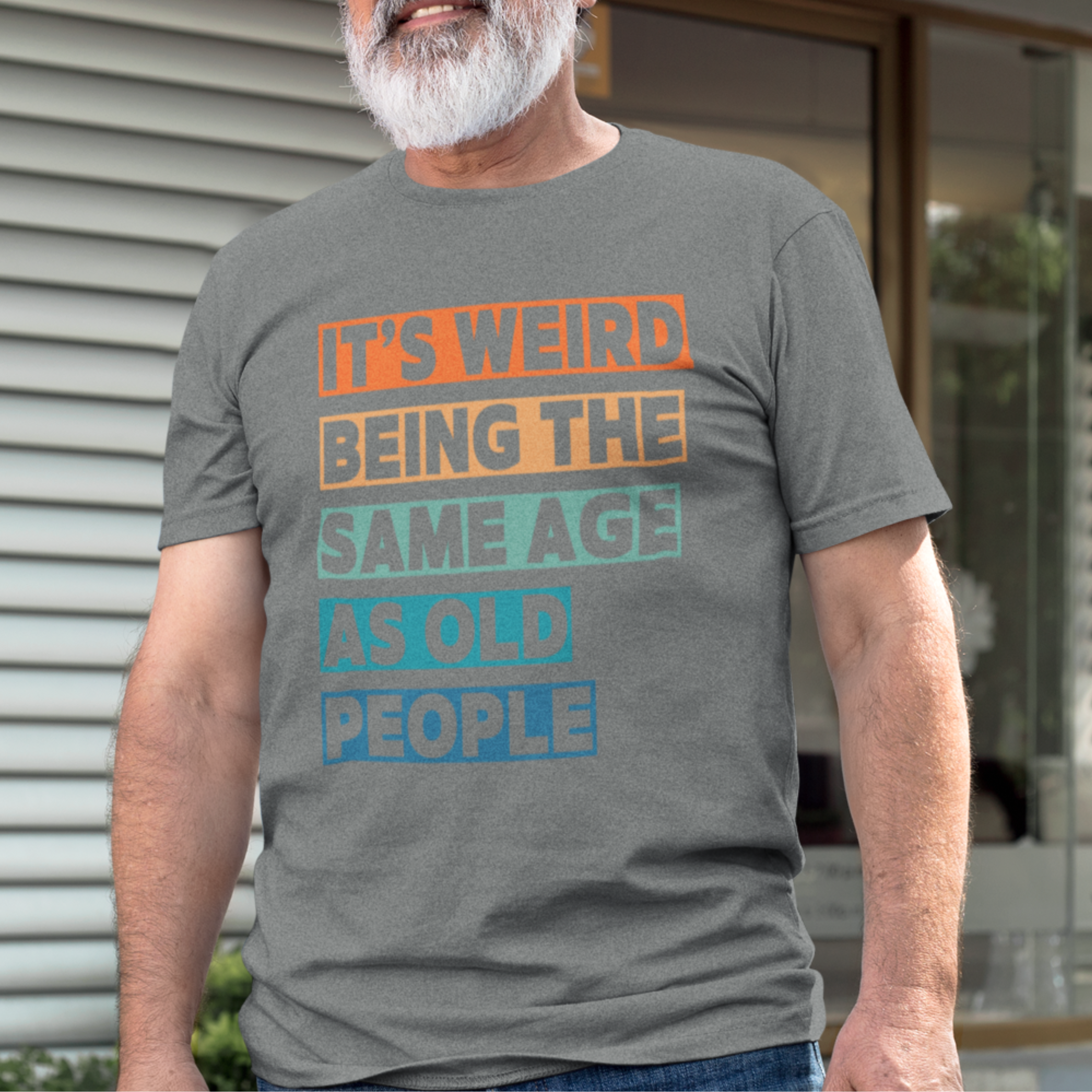 Gray tee featuring bold, multi-color block lettering reads It’s Weird Being the Same Age as Old People 