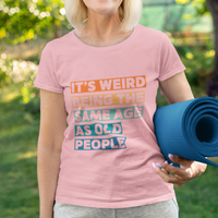 Pink tee featuring bold, multi-color block lettering reads It’s Weird Being the Same Age as Old People 