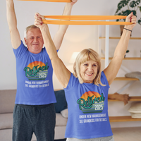 A couple in royal blue t-shirts featuring a rainbow striped sun that reads Retired 2025 Under New Management See Grandkids for Details.