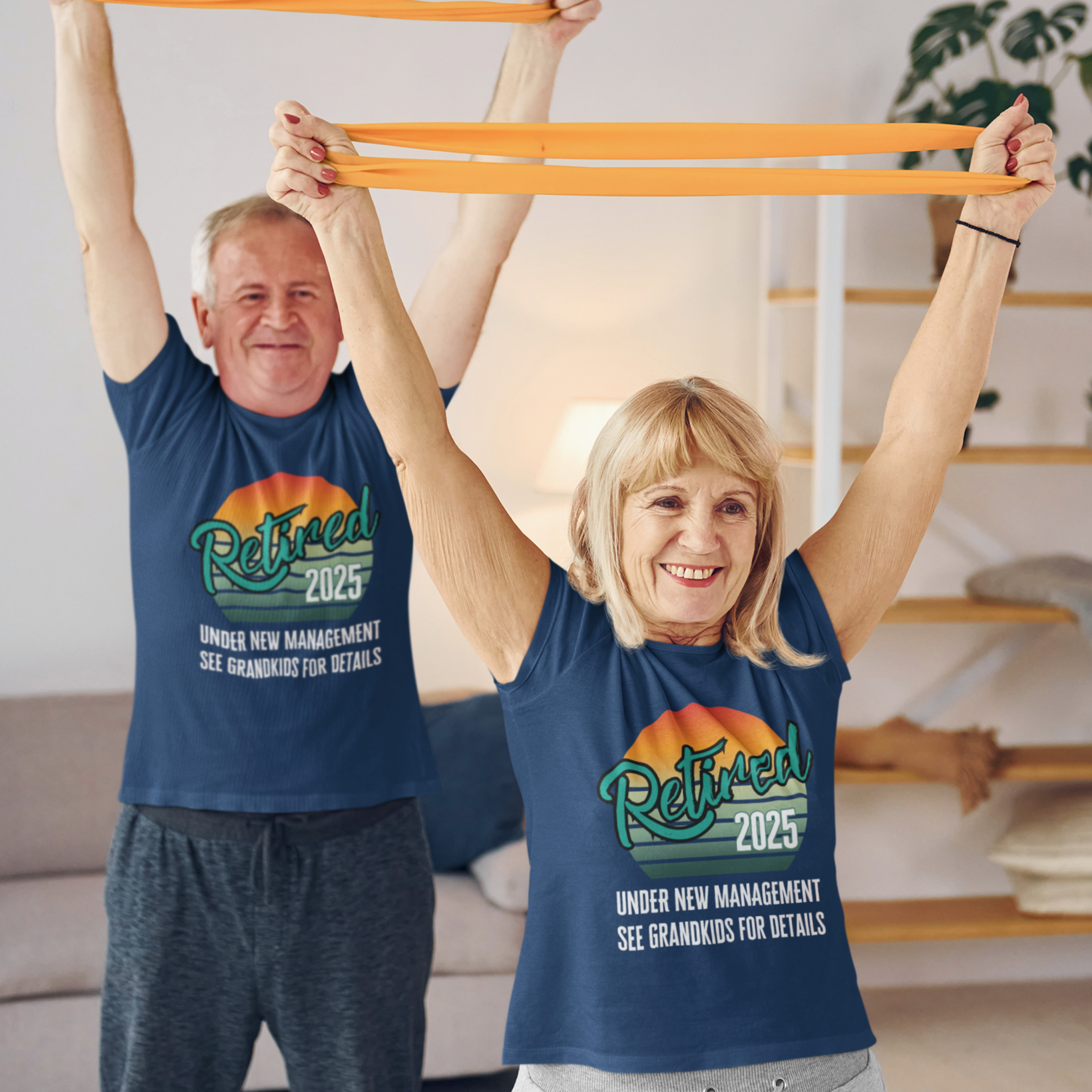 A couple in navy blue t-shirts featuring a rainbow striped sun that reads Retired 2025 Under New Management See Grandkids for Details.