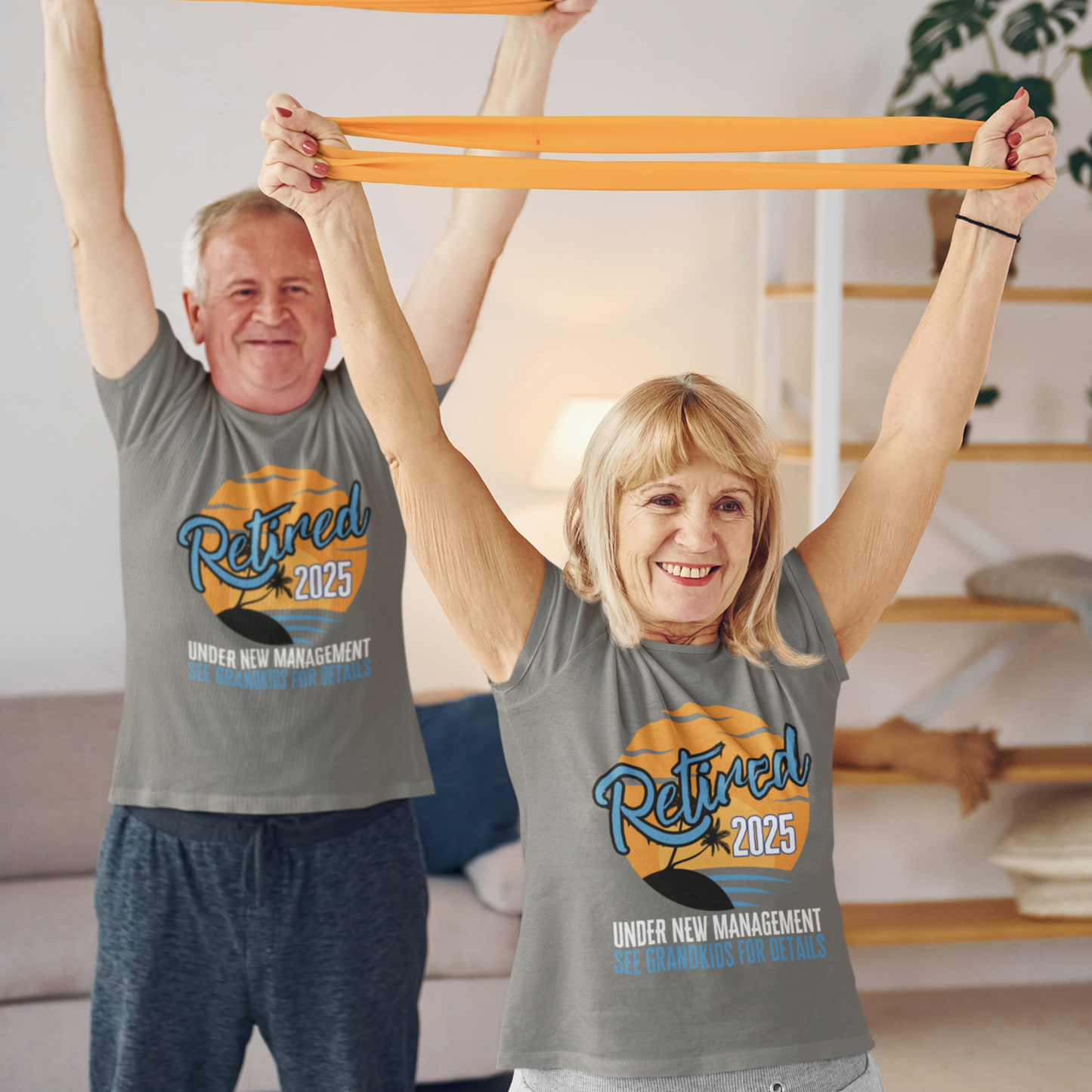 A couple in gray t-shirts featuring a sunset beach scene that reads Retired 2025 Under New Management See Grandkids for Details.