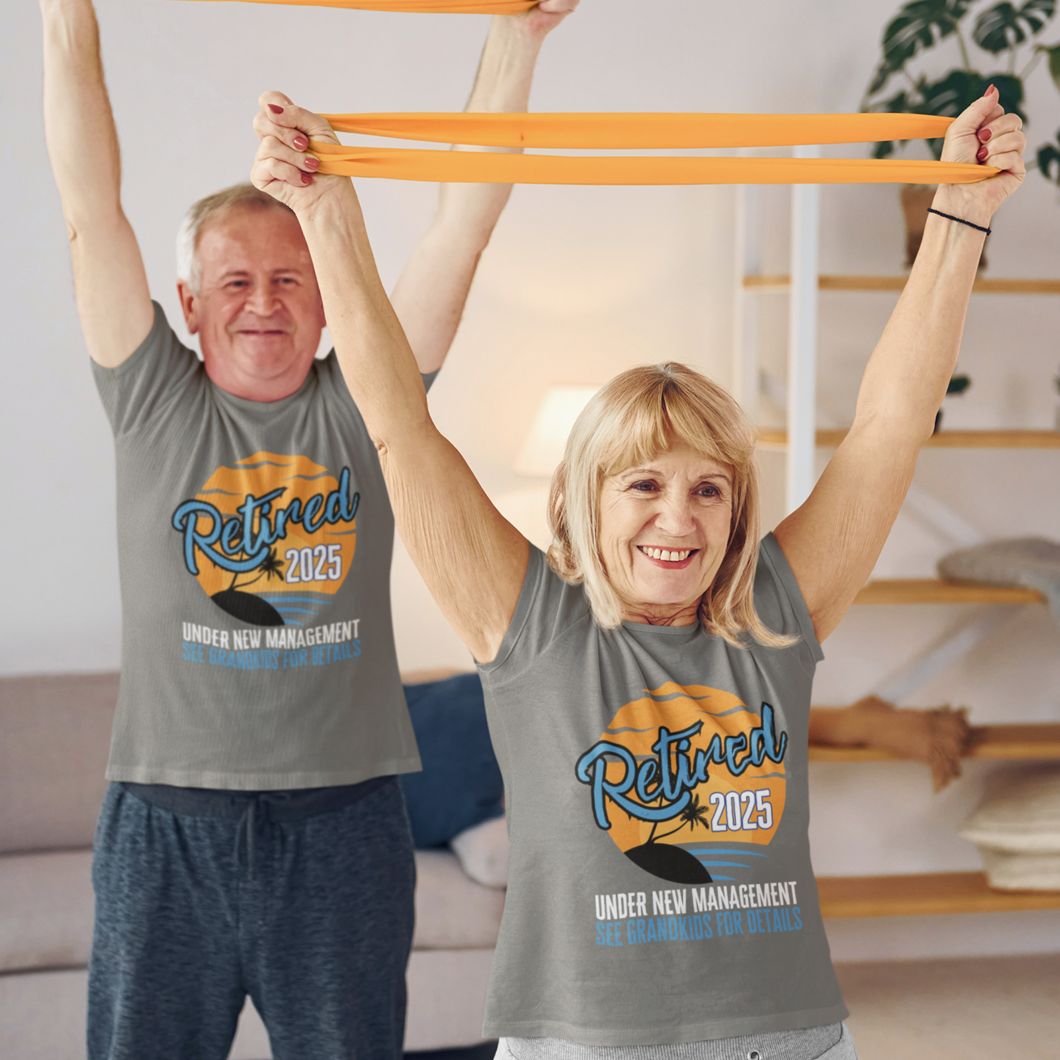 A couple in gray t-shirts featuring a sunset beach scene that reads Retired 2025 Under New Management See Grandkids for Details.