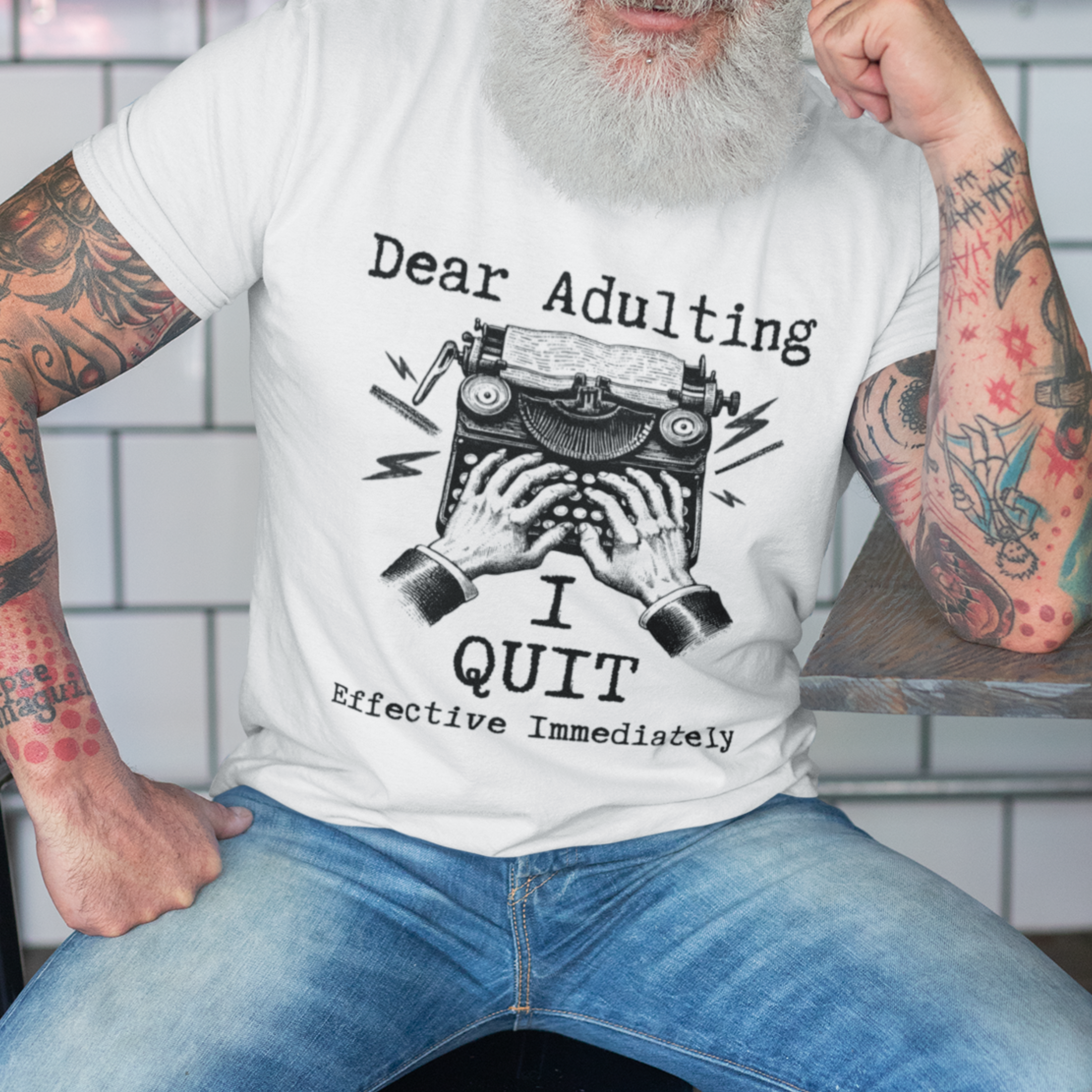 White t-shirt featuring a man's hand typing out his resignation letter to Adulting on an old typewriter