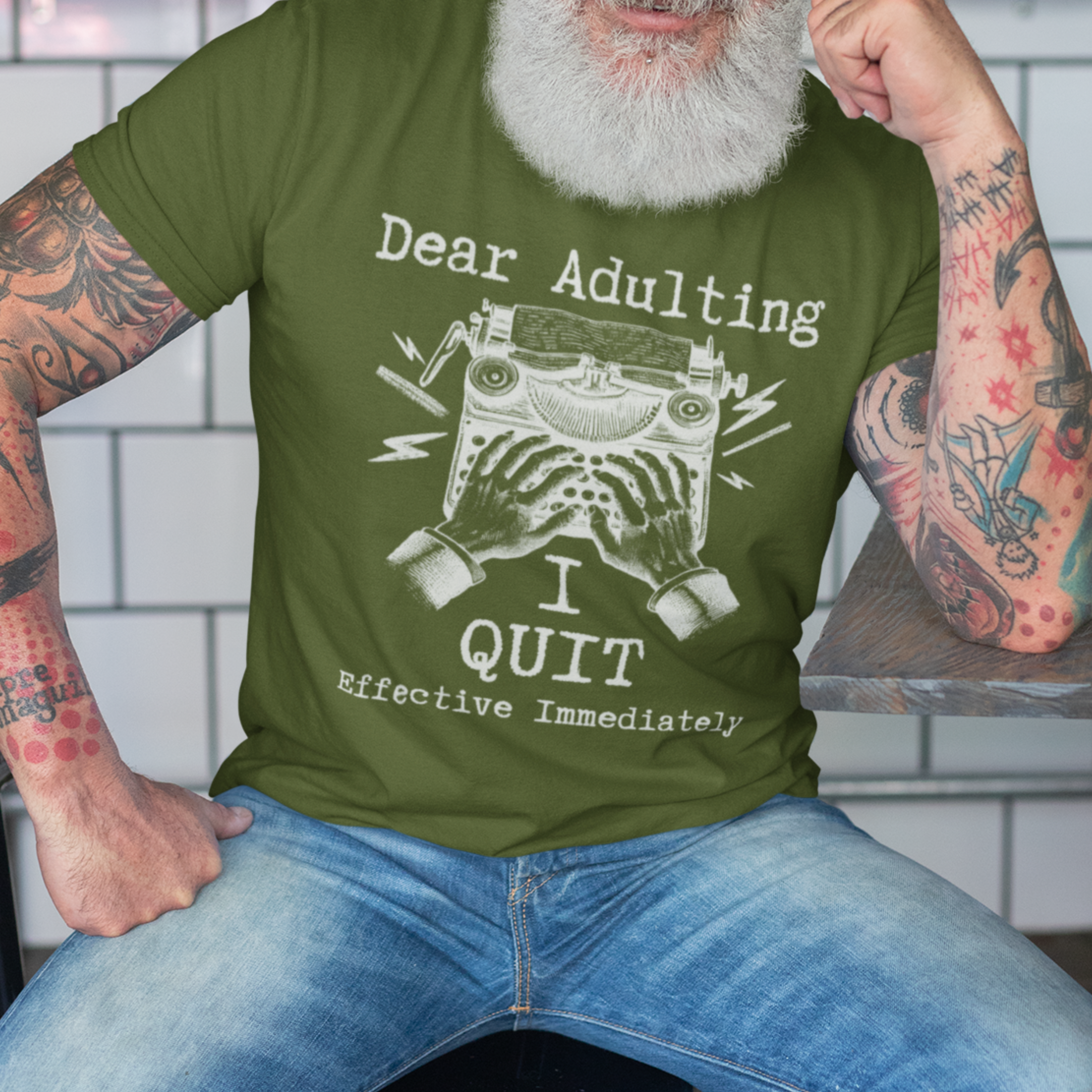 Military green t-shirt featuring a man's hand typing out his resignation letter to Adulting on an old typewriter