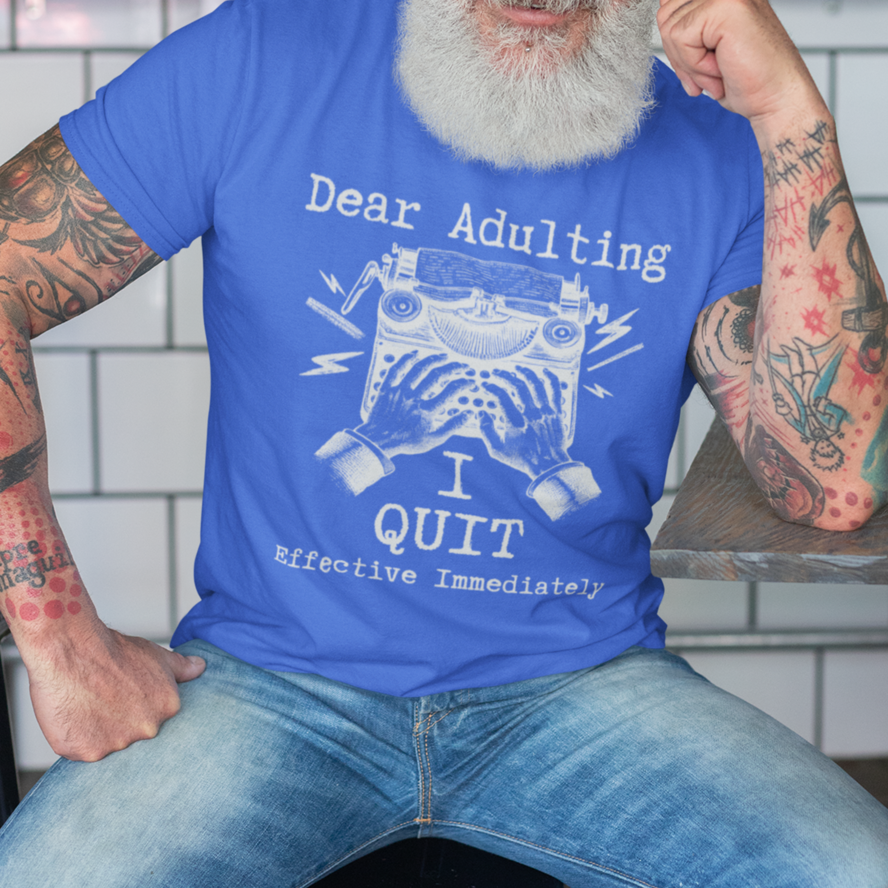 Royal blue t-shirt featuring a man's hand typing out his resignation letter to Adulting on an old typewriter