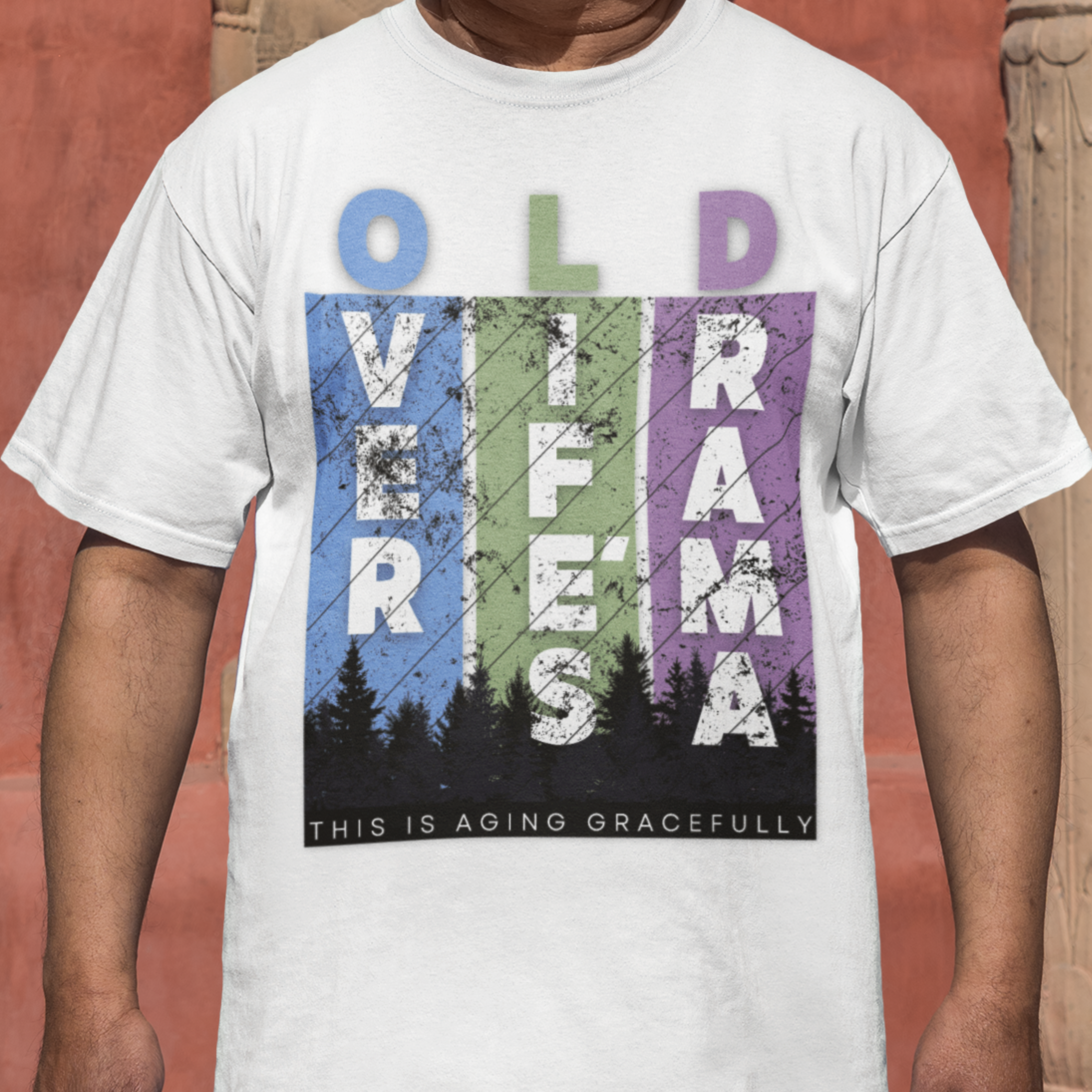 White t-shirt featuring pastel stripes and lettering with a forest scene in silhouette, stating Over Life's Drama This is Aging Gracefully