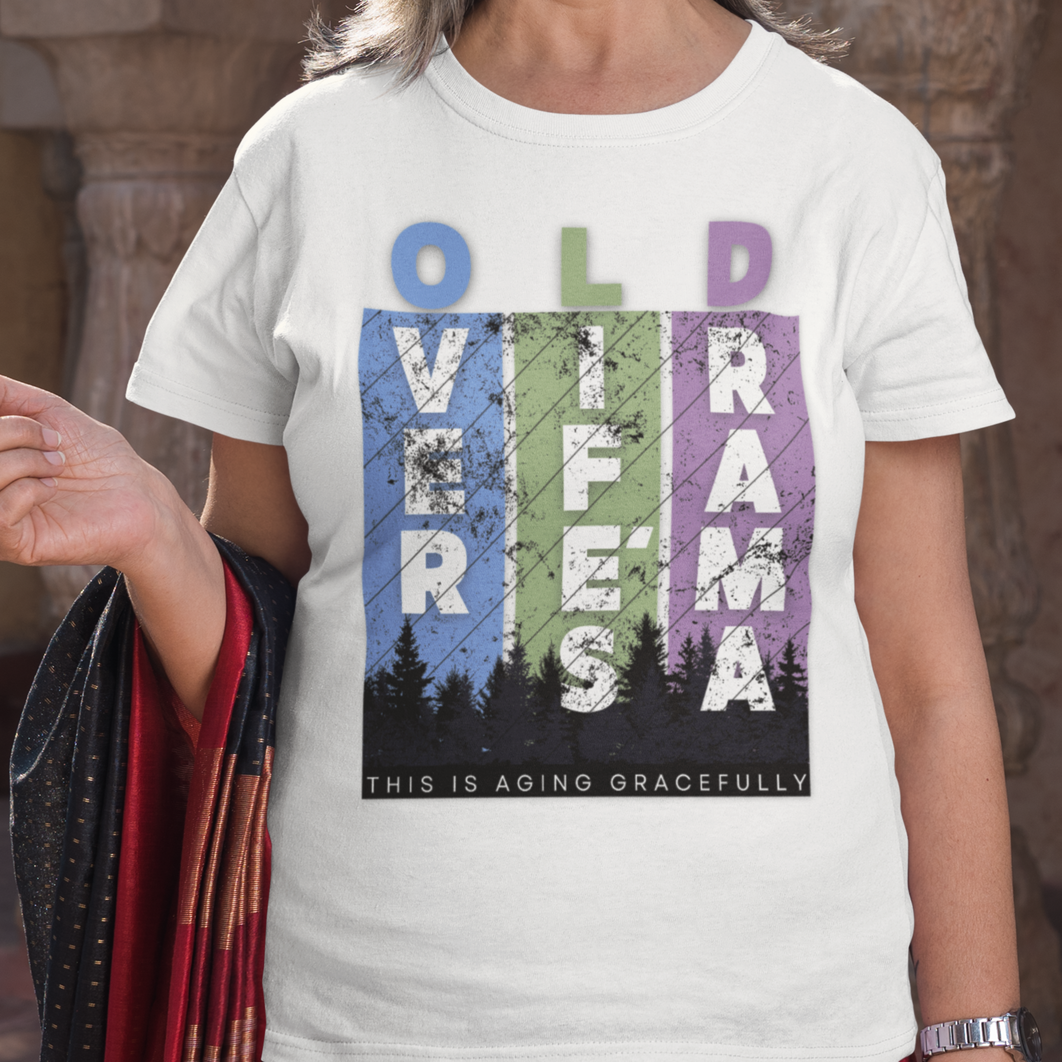 White t-shirt featuring pastel stripes and lettering with a forest scene in silhouette, stating Over Life's Drama This is Aging Gracefully