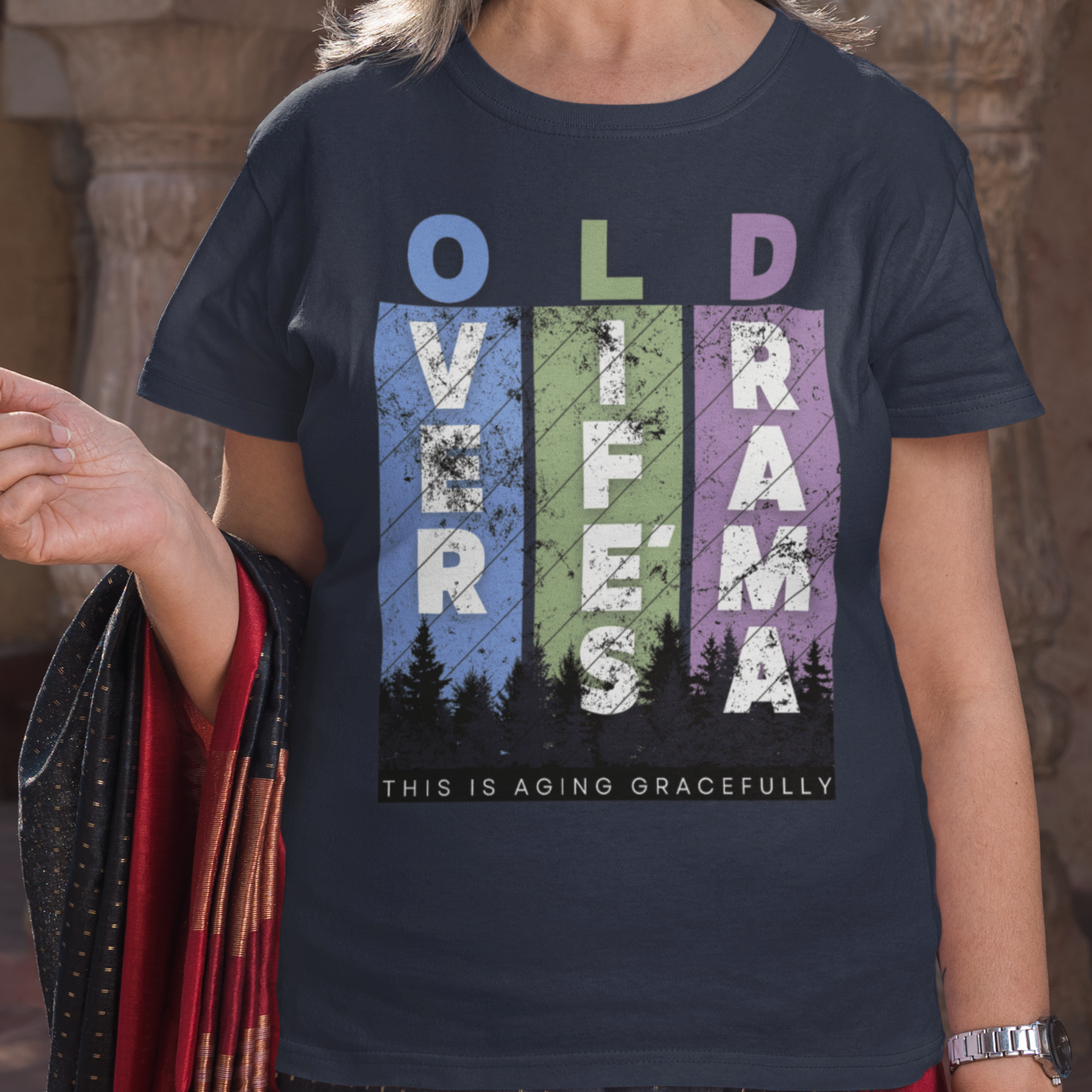 Navy blue t-shirt featuring pastel stripes and lettering with a forest scene in silhouette, stating Over Life's Drama This is Aging Gracefully