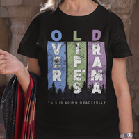 Black t-shirt featuring pastel stripes and lettering with a forest scene in silhouette, stating Over Life's Drama This is Aging Gracefully