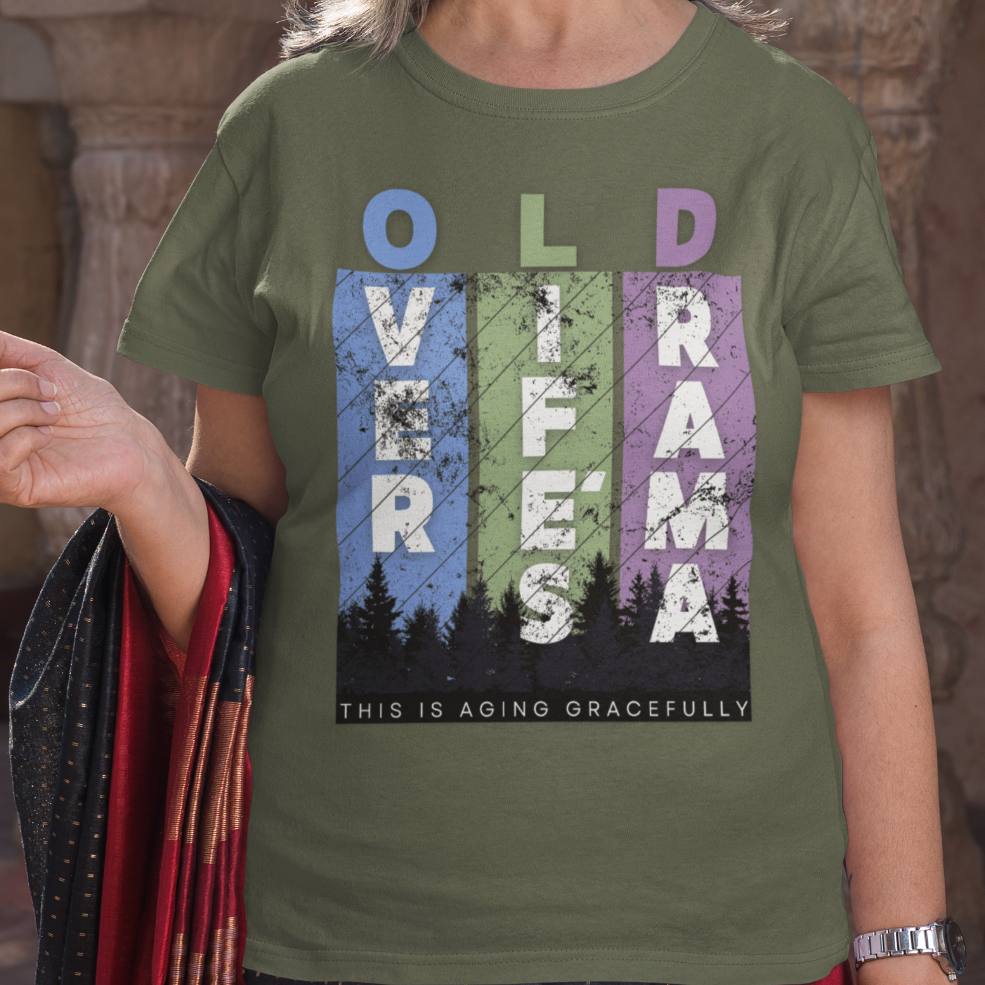 Military green t-shirt featuring pastel stripes and lettering with a forest scene in silhouette, stating Over Life's Drama This is Aging Gracefully