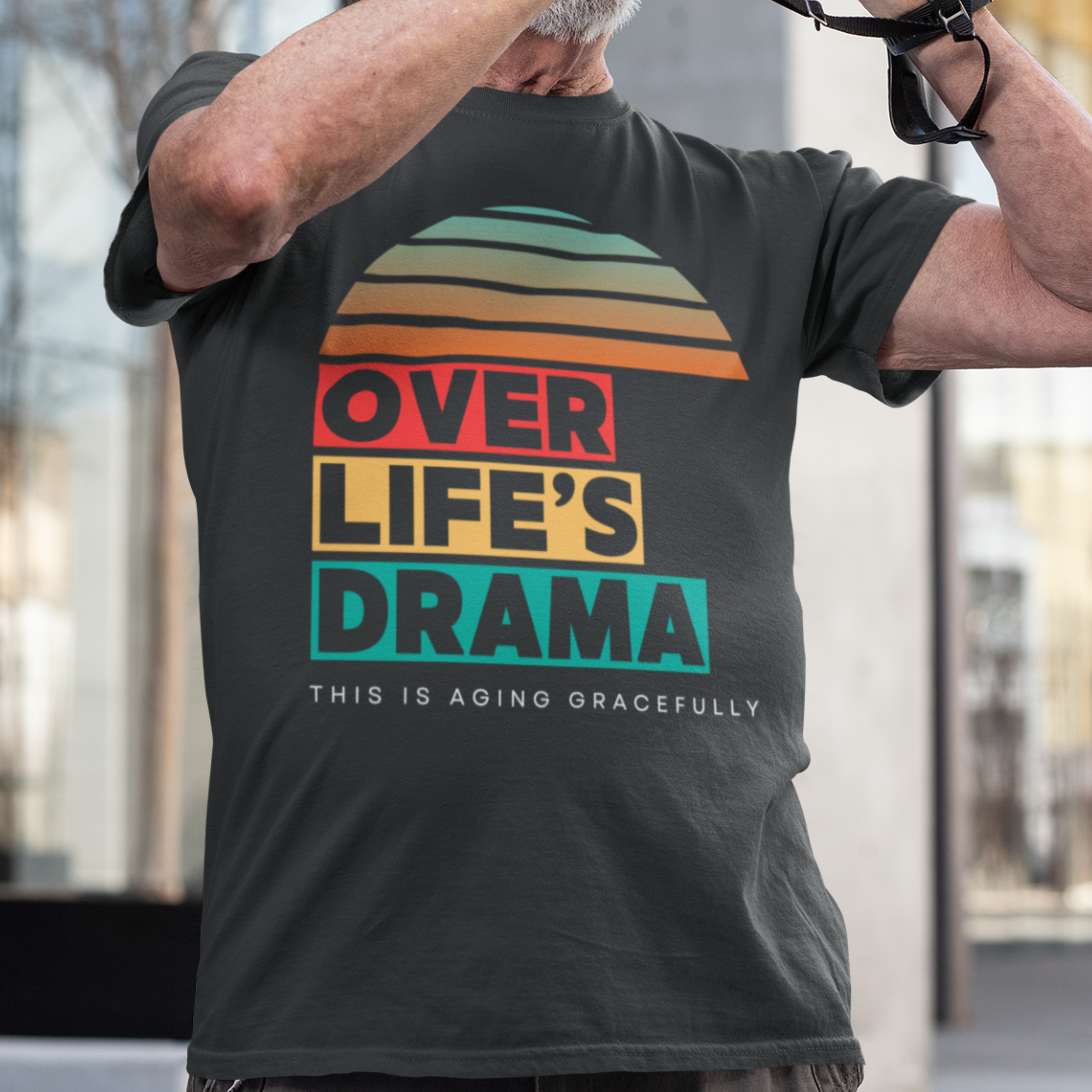 Black t-shirt that reads Over Life's Drama This is Aging Gracefully, featuring colorful block lettering and a rainbow striped sunset.