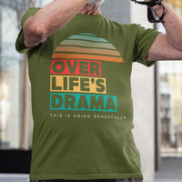 Military green t-shirt that reads Over Life's Drama This is Aging Gracefully, featuring colorful block lettering and a rainbow striped sunset.