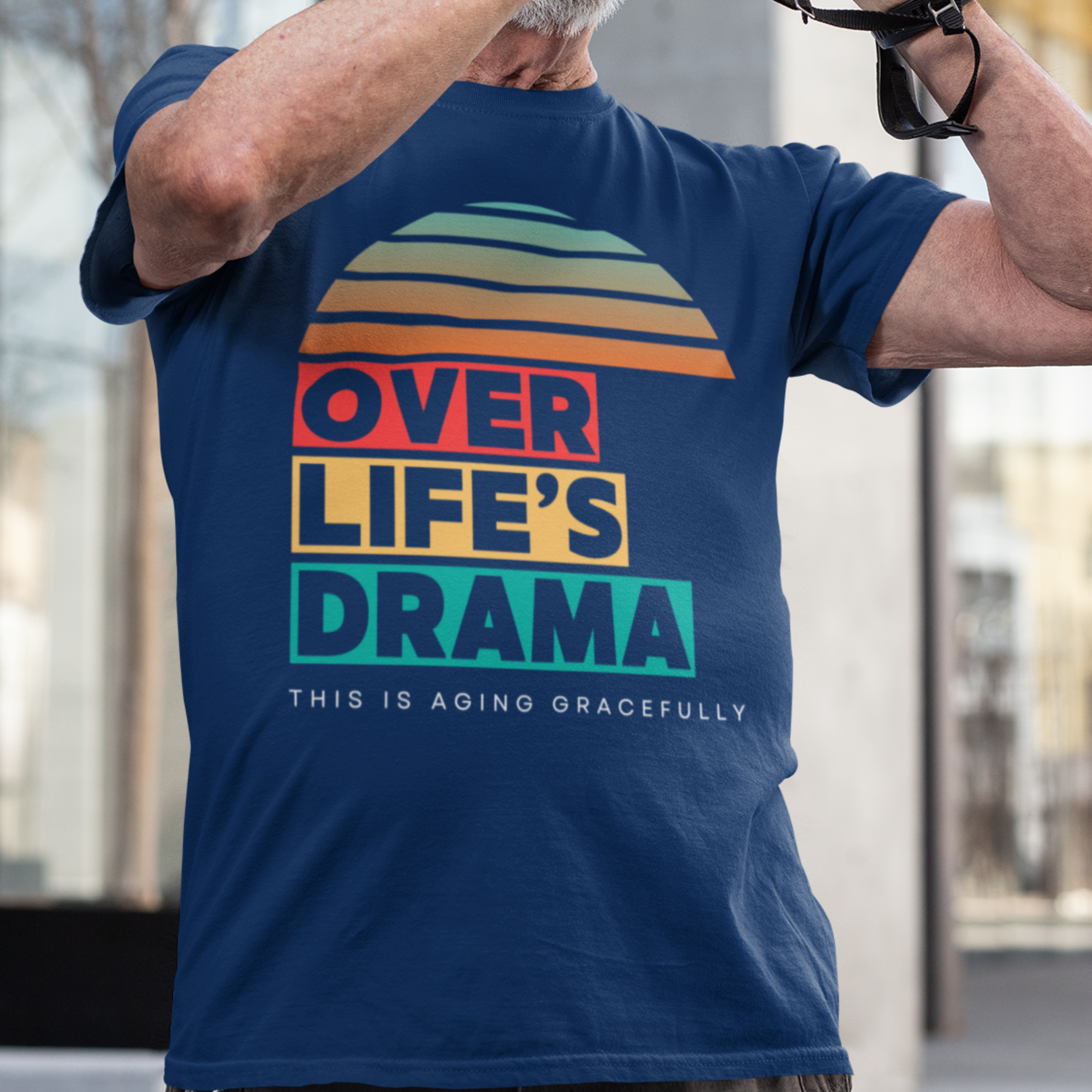 Navy blue t-shirt that reads Over Life's Drama This is Aging Gracefully, featuring colorful block lettering and a rainbow striped sunset.