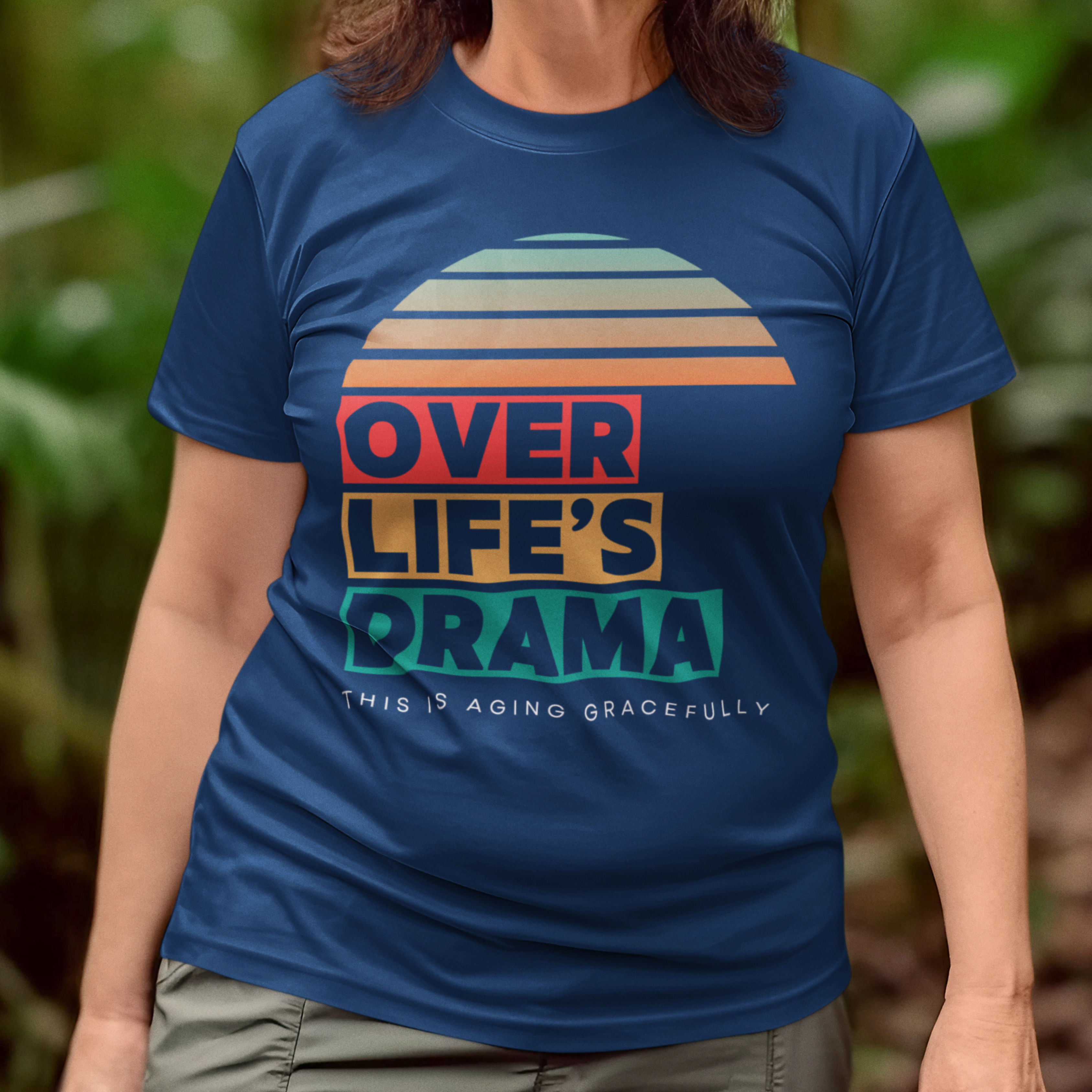 Navy blue t-shirt that reads Over Life's Drama This is Aging Gracefully, featuring colorful block lettering and a rainbow striped sunset.