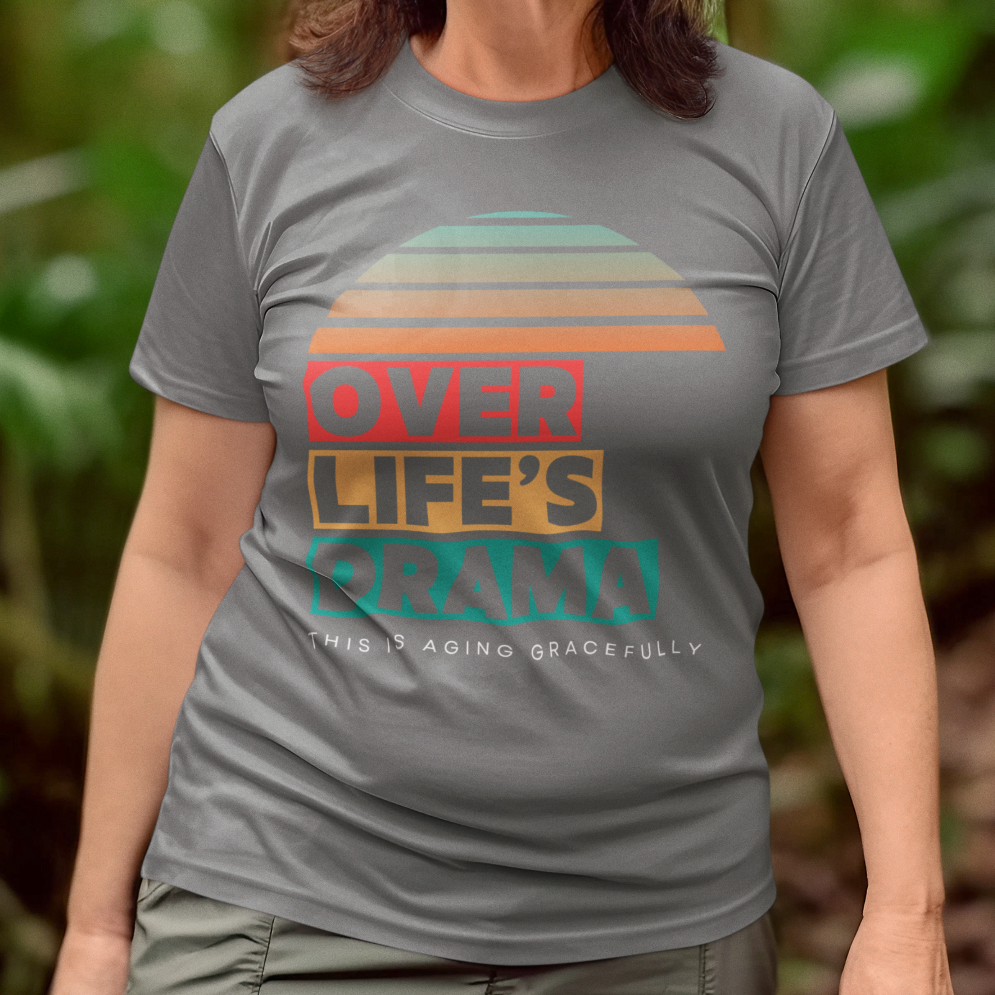 Gray t-shirt that reads Over Life's Drama This is Aging Gracefully, featuring colorful block lettering and a rainbow striped sunset.