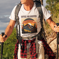White tee on a male hiker featuring a mountain peak at sunset in warm colors that reads Office Relocated No Forwarding Address Provided