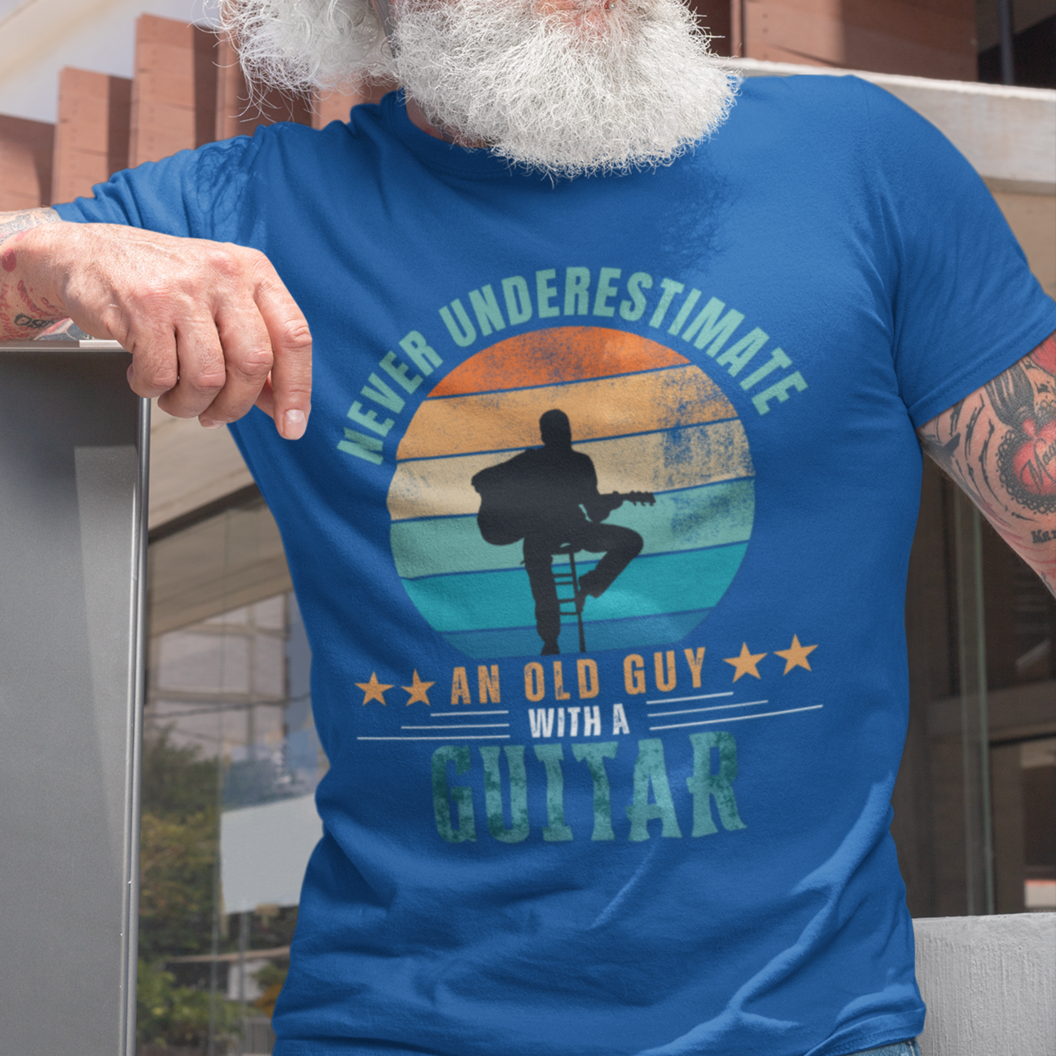 Royal blue tee featuring silhouette of a guy on a stool playing a guitar against a distressed striped sunset