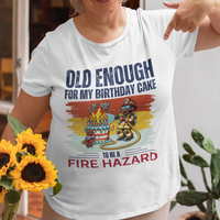 White tee featuring a cartoon fireman putting out the flames from the candles on a birthday cake.