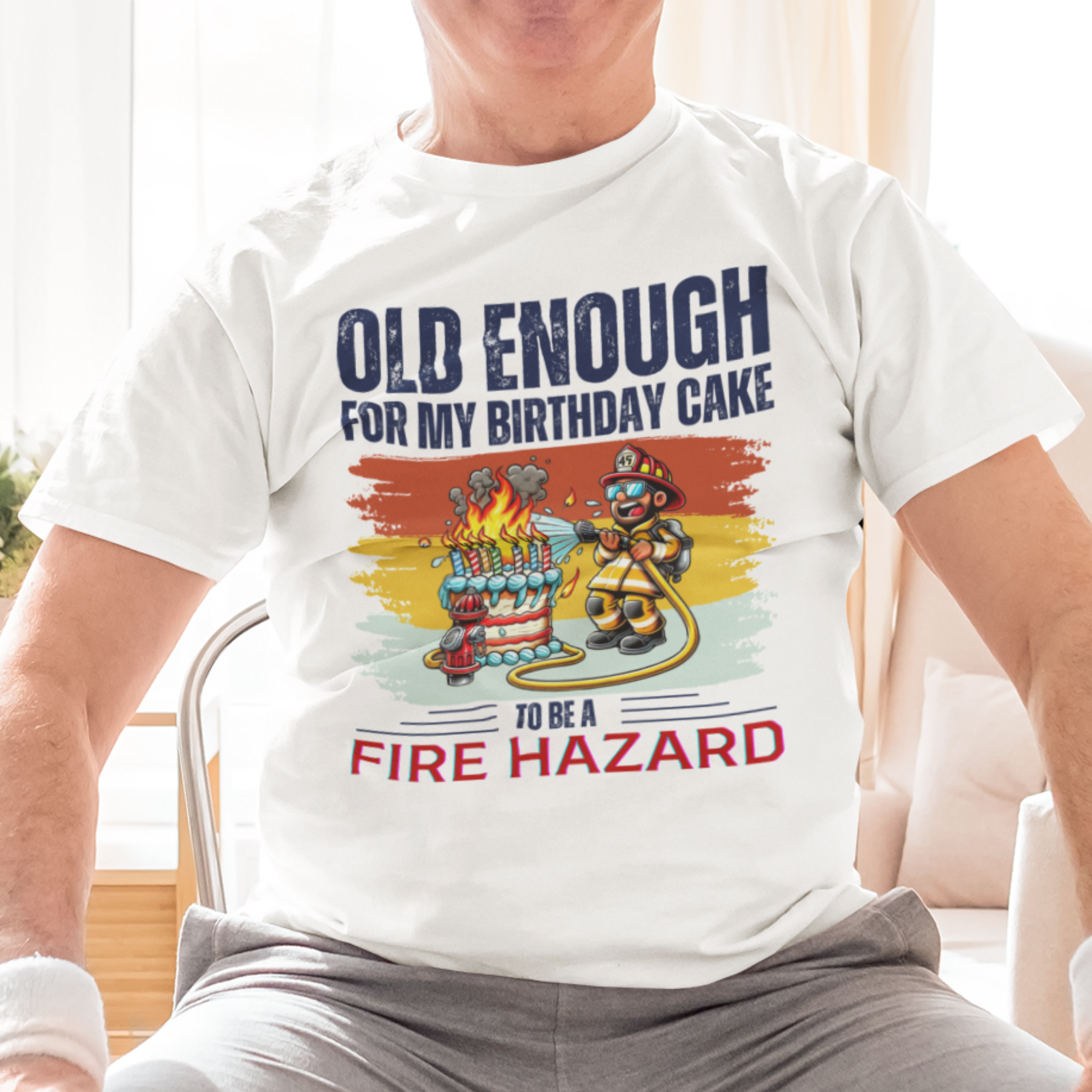White tee featuring a cartoon fireman putting out the flames from the candles on a birthday cake.