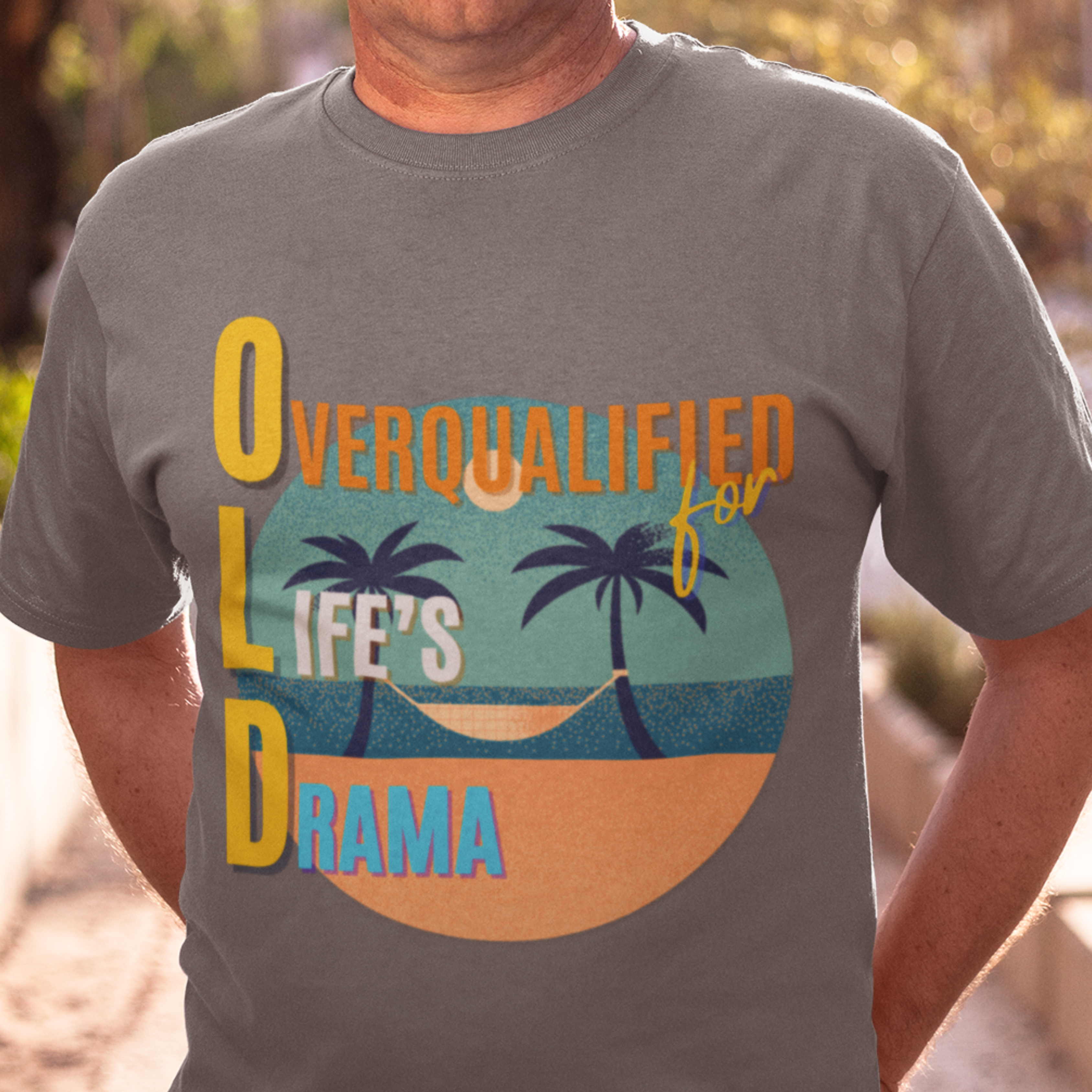 Heather gray tee featuring a hammock between two palm trees on a secluded beach, reading "OLD: Overqualified for Life's Drama"
