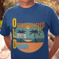 Royal blue tee featuring a hammock between two palm trees on a secluded beach, reading "OLD: Overqualified for Life's Drama"